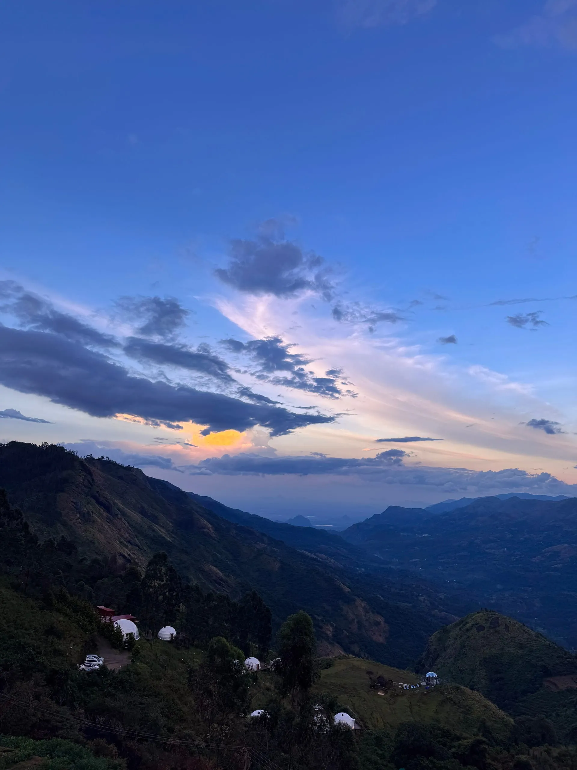 Blue hour over the valley, with dome tents and a few buildings on the near hillside and the plains far below